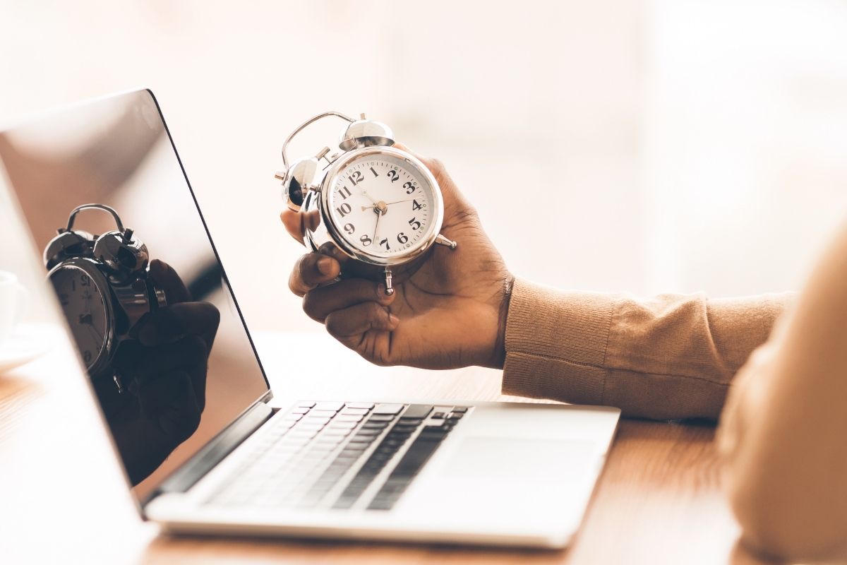 Student holding an alarm clock next to a laptop, symbolizing SAT time management during digital test prep.